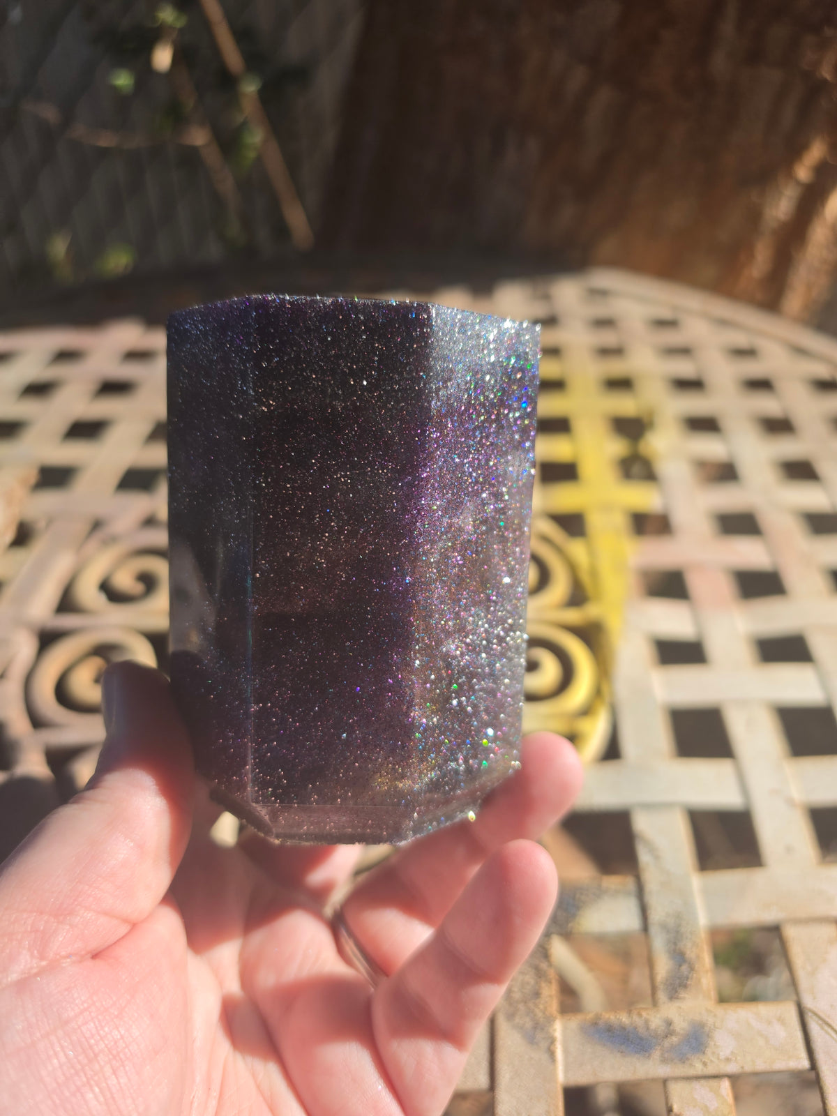Hand holding midnight purple hexagonal resin dice cup showing full holographic glitter exterior in sunlight