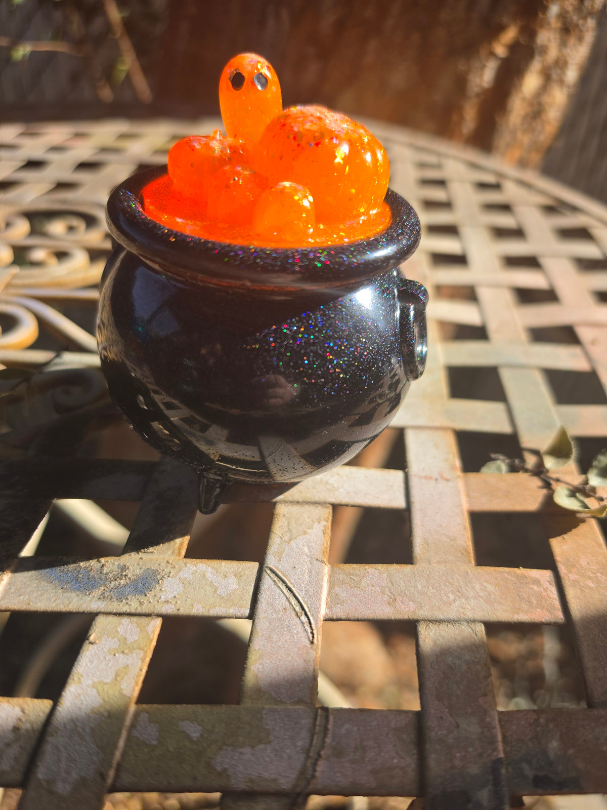 Cauldron sitting on lattice table showing full pumpkin ghost lid and black glitter base