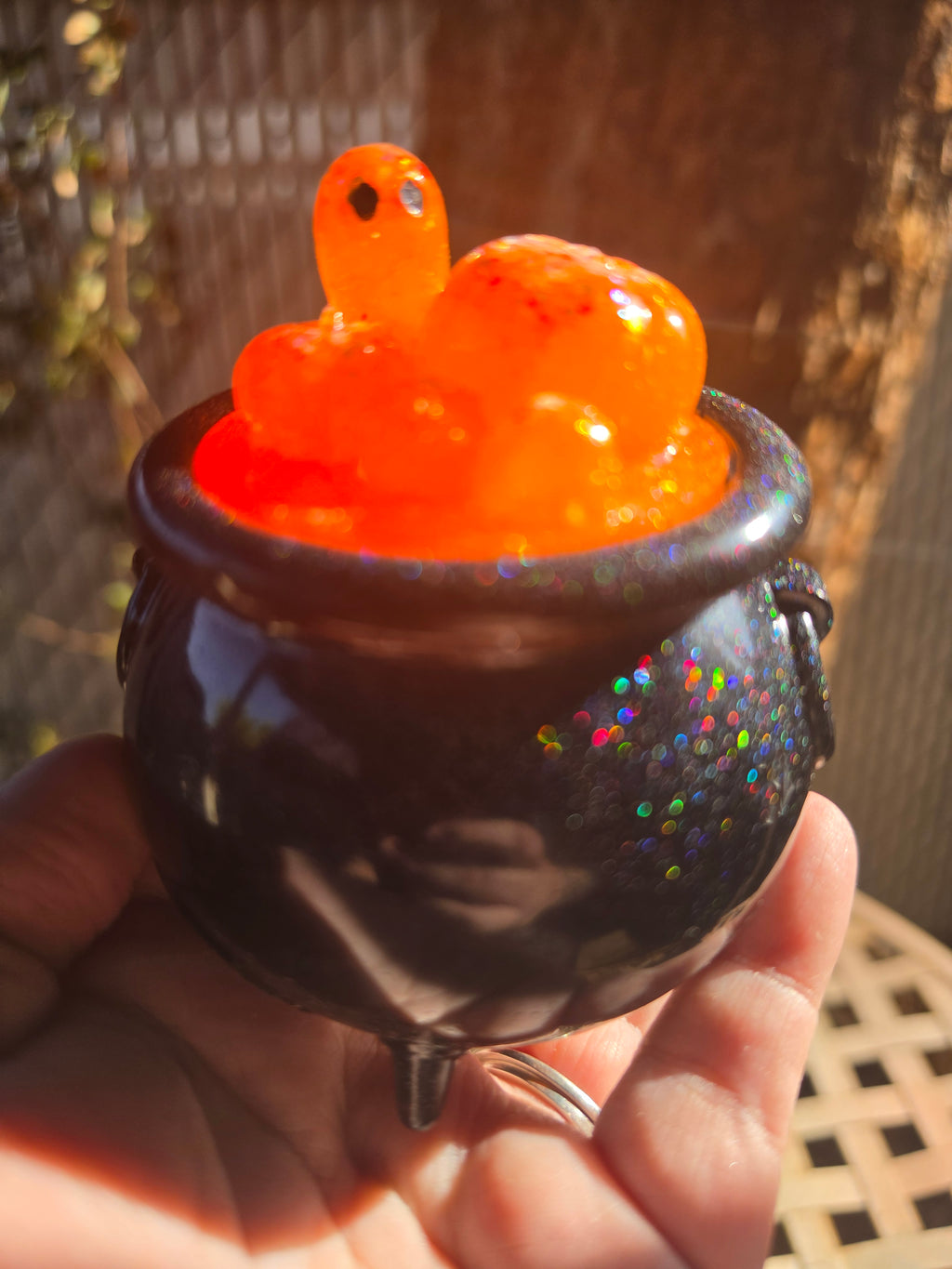 Black galaxy glitter resin cauldron with orange pumpkin bubble lid and ghost figure, held in hand outdoors