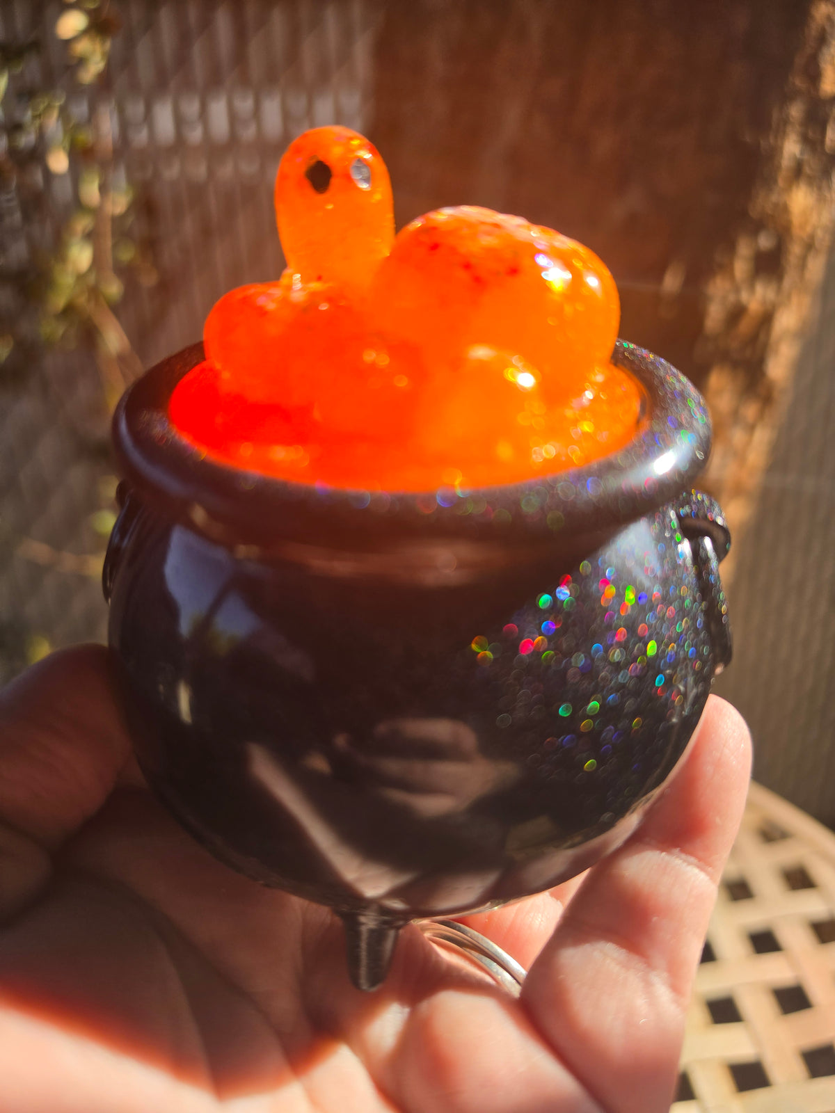 Black galaxy glitter resin cauldron with orange pumpkin bubble lid and ghost figure, held in hand outdoors