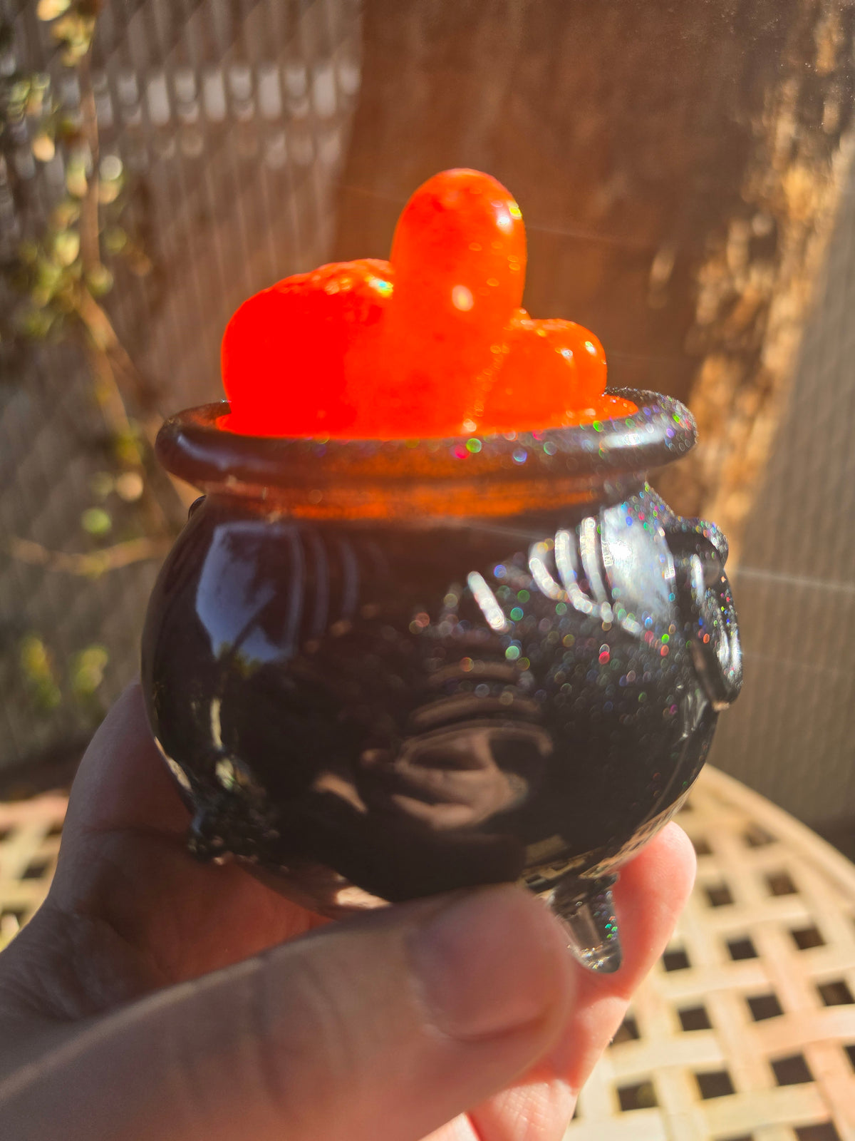 Hand holding black resin cauldron showing orange pumpkin clusters with ghost emerging from lid