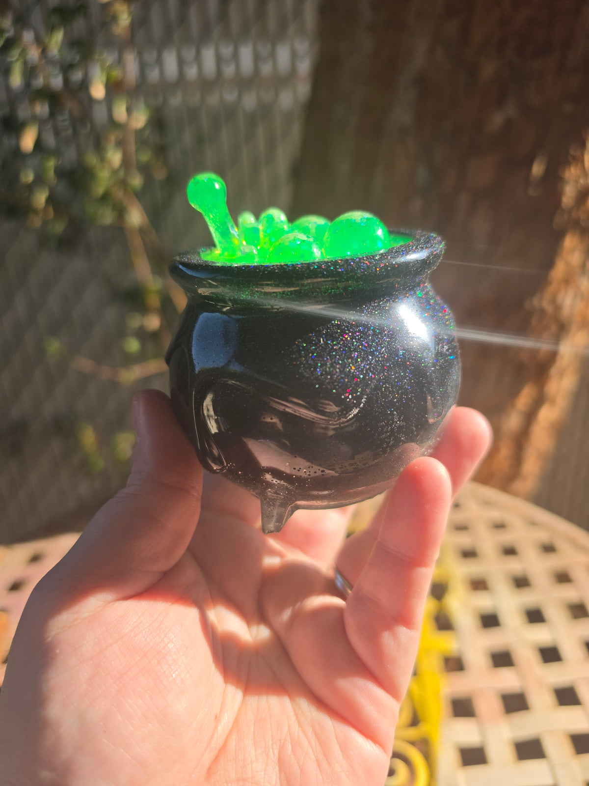 Black galaxy glitter resin cauldron with neon green bubbling resin lid held up in sunlight