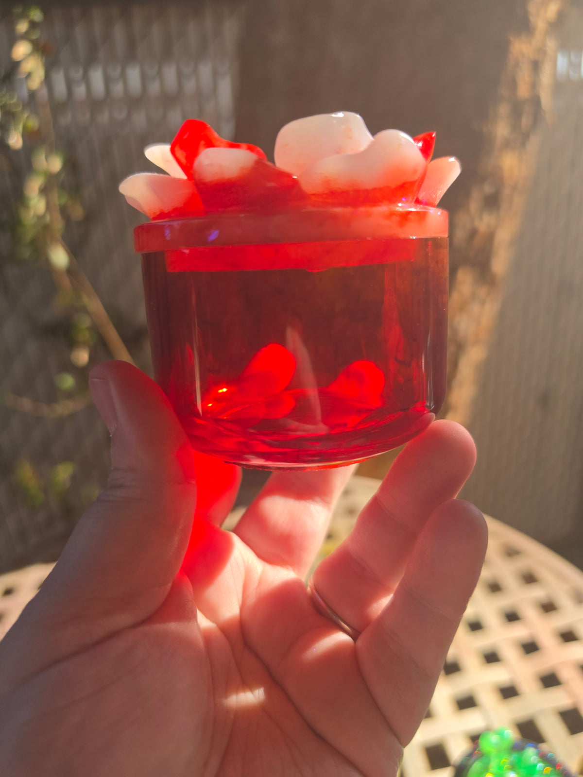 Deep crimson translucent resin jar with white and red floral resin lid, held up to sunlight