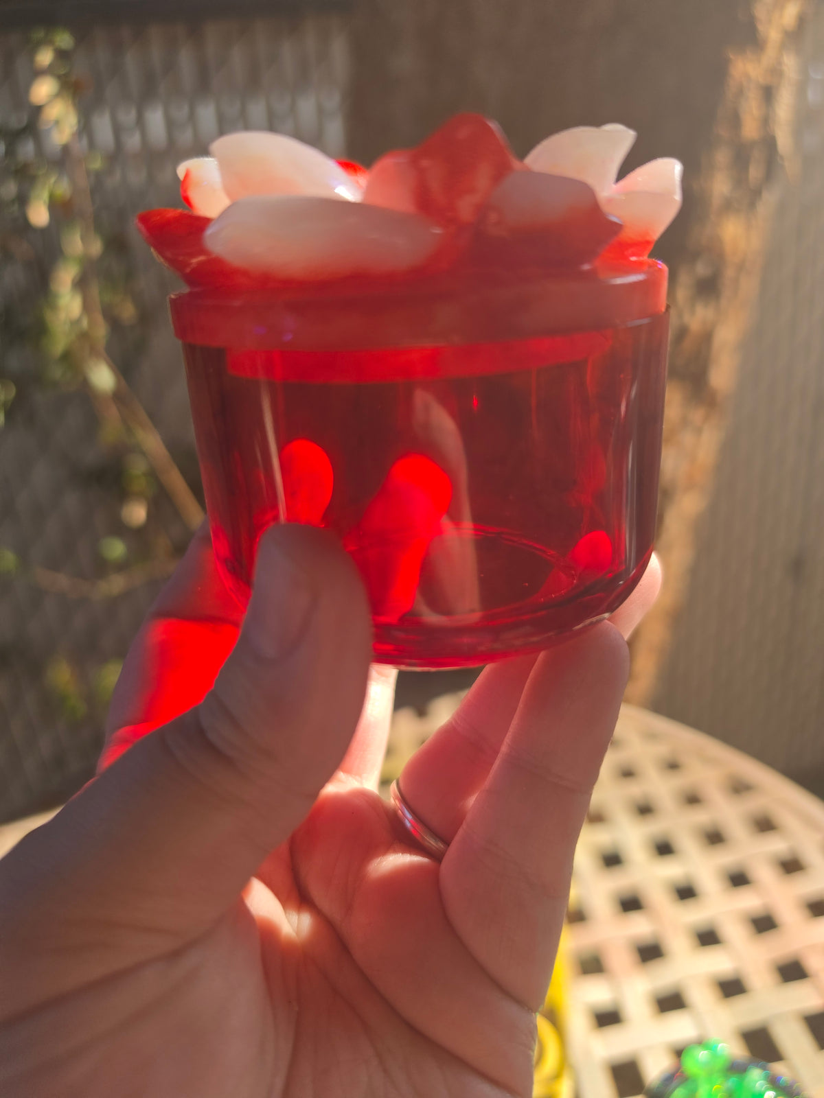 Crimson resin jar with lid removed, sitting on lattice table outdoors