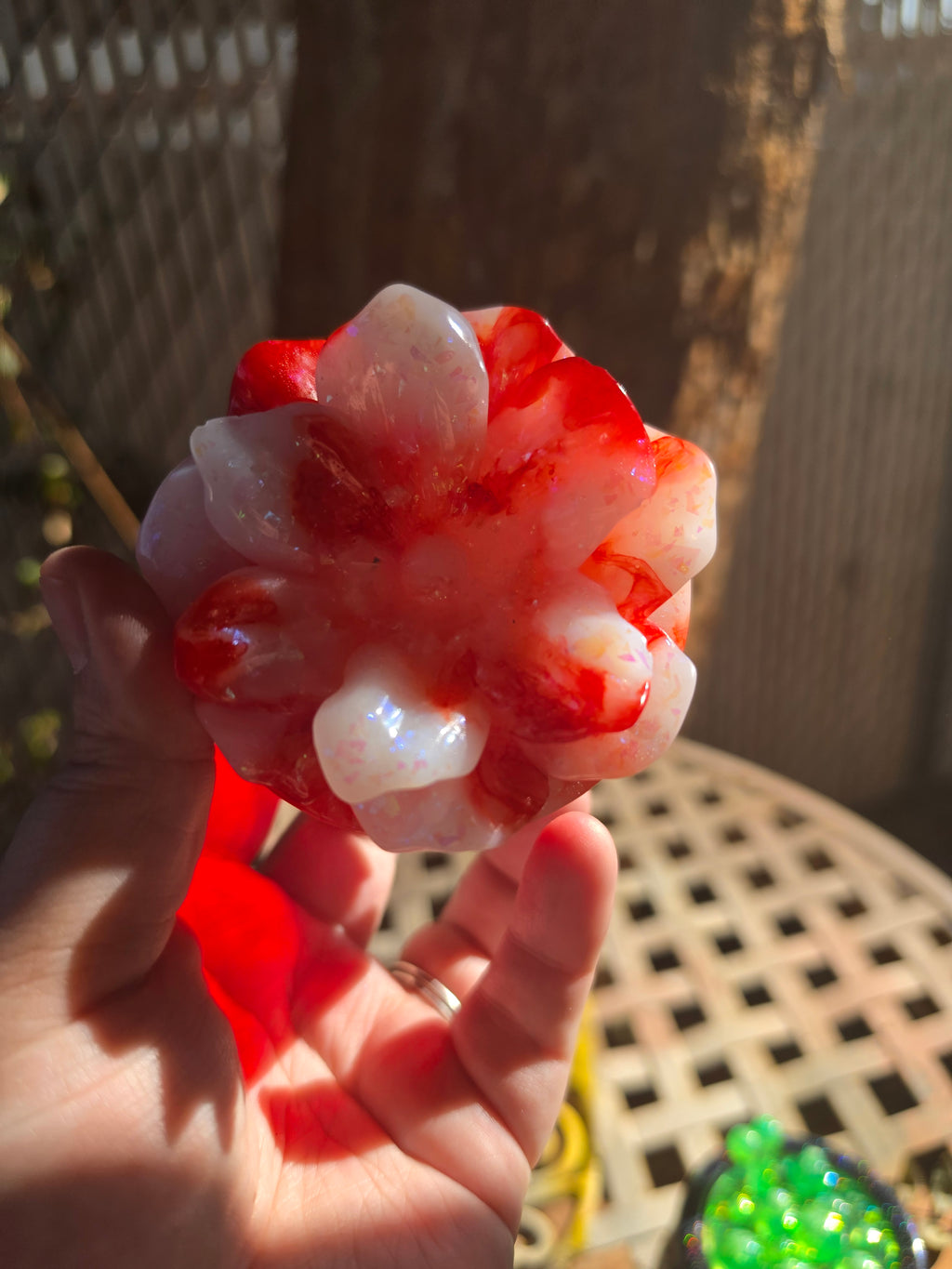 Side view of crimson resin jar with flower lid outdoors in sunlight