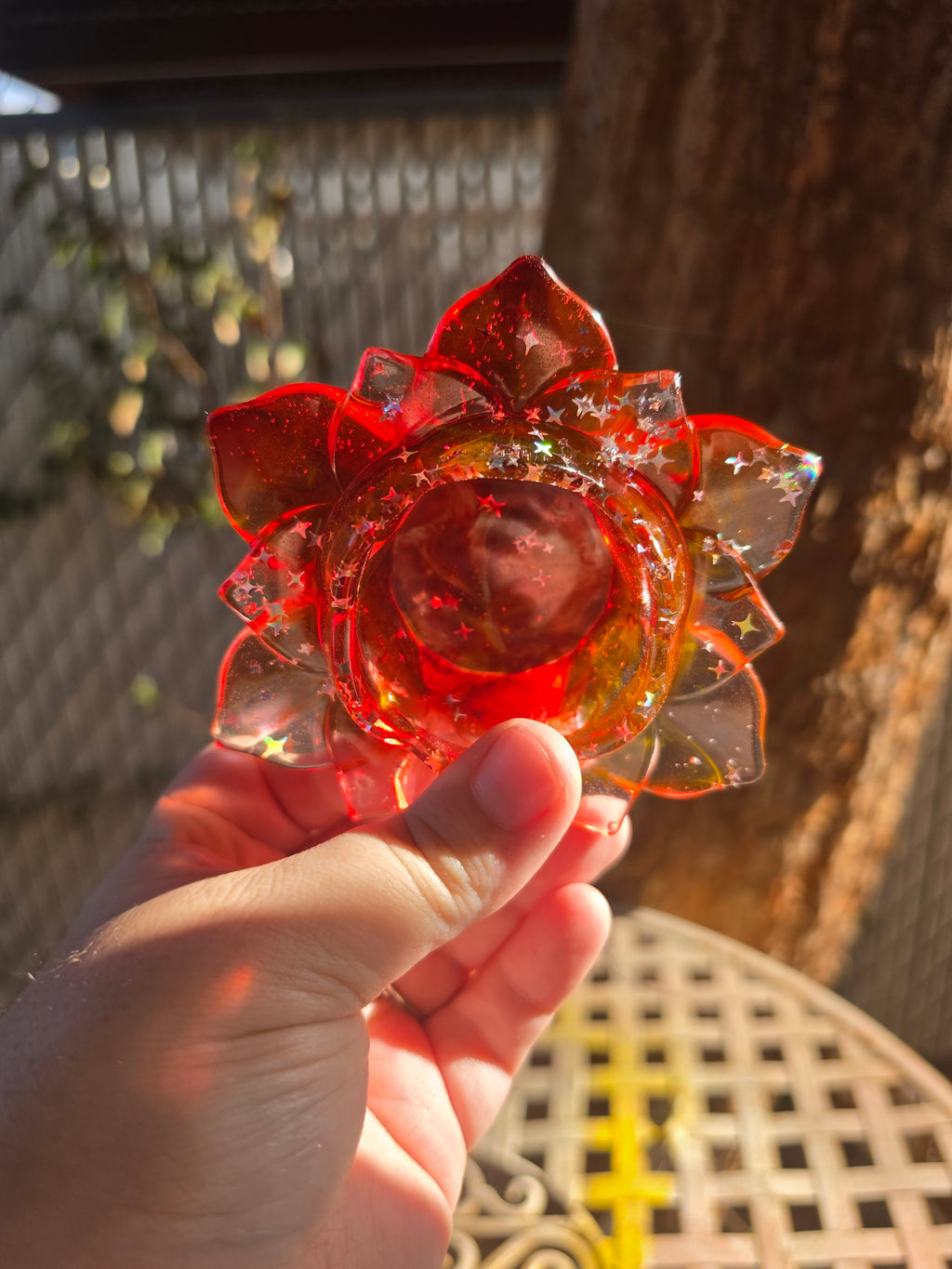 Hand holding lotus resin dish from below showing amber red gradient and star glitter suspension