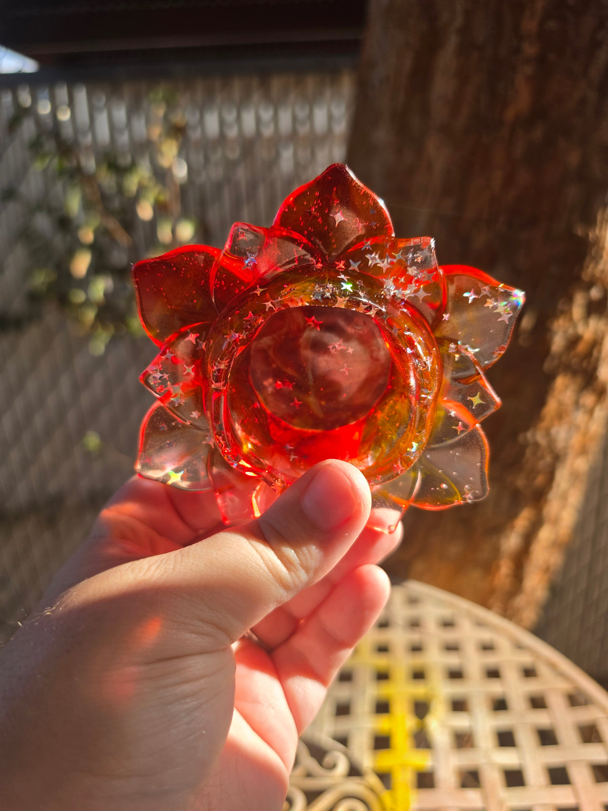 Hand holding lotus resin dish from below showing amber red gradient and star glitter suspension