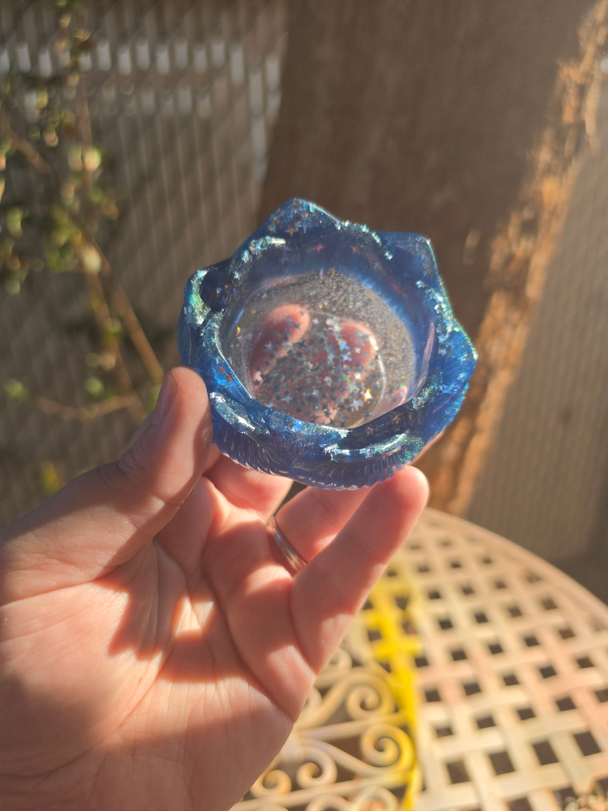 Cobalt blue and violet galaxy lotus resin dice throne held in sunlight showing iridescent star glitter in bowl