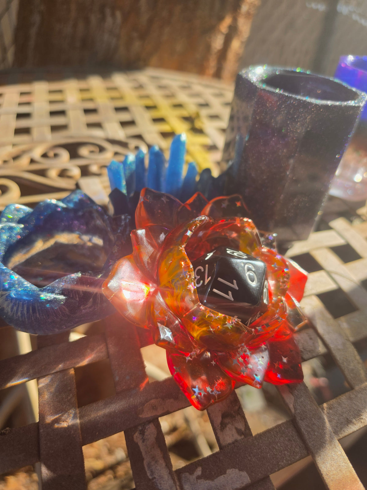 Crimson and amber translucent resin lotus flower dice throne held in sunlight showing star glitter